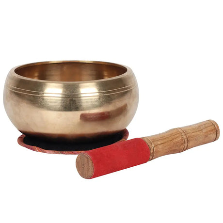 Brass singing bowl on red cushion with wooden striker, perfect for meditation practices