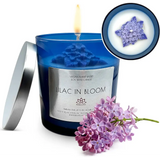 Blue scented soy candle labeled Lilac in Bloom with lilac flowers beside it