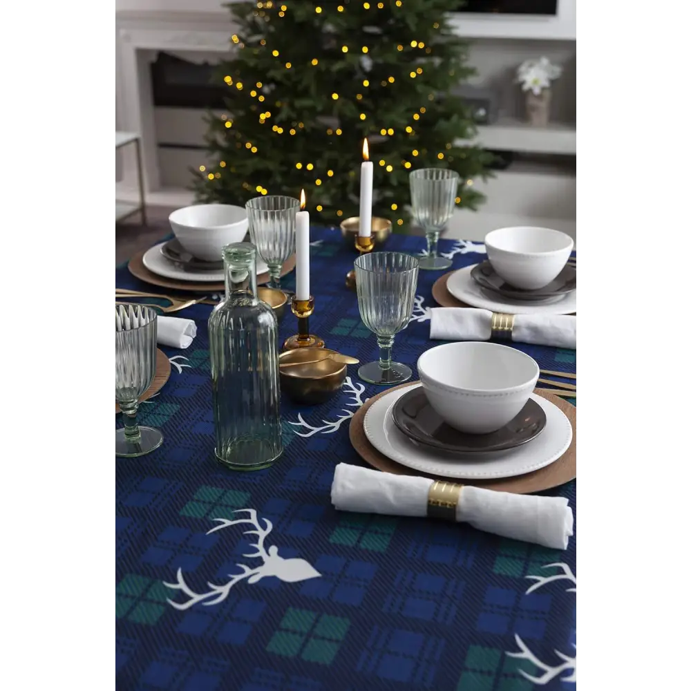 Festive dining table with Christmas tablecloth, white dishes, and a glowing tree backdrop