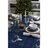 Festive dining table with Christmas tablecloth, white dishes, and a glowing tree backdrop