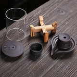 Traditional Chinese tea set with a black clay teapot and glass cup on a wooden holder