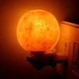 Glowing Himalayan Salt Lamp with warm white glow plugged into a wall outlet