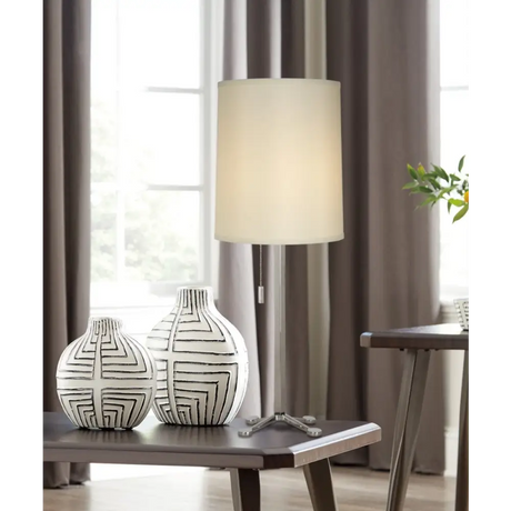 Two white ceramic vases with black geometric lines beside a polished chrome table lamp