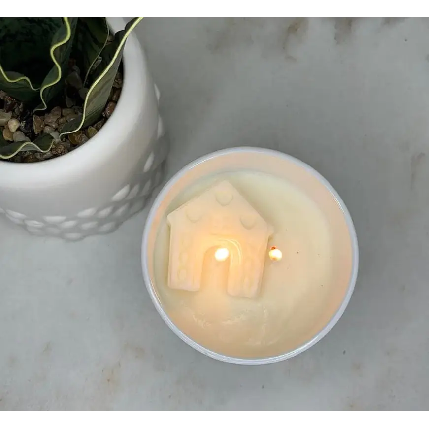 Lit candle in white ceramic holder with house design, perfect for a happy place scented atmosphere