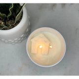 Lit candle in white ceramic holder with house design, perfect for a happy place scented atmosphere