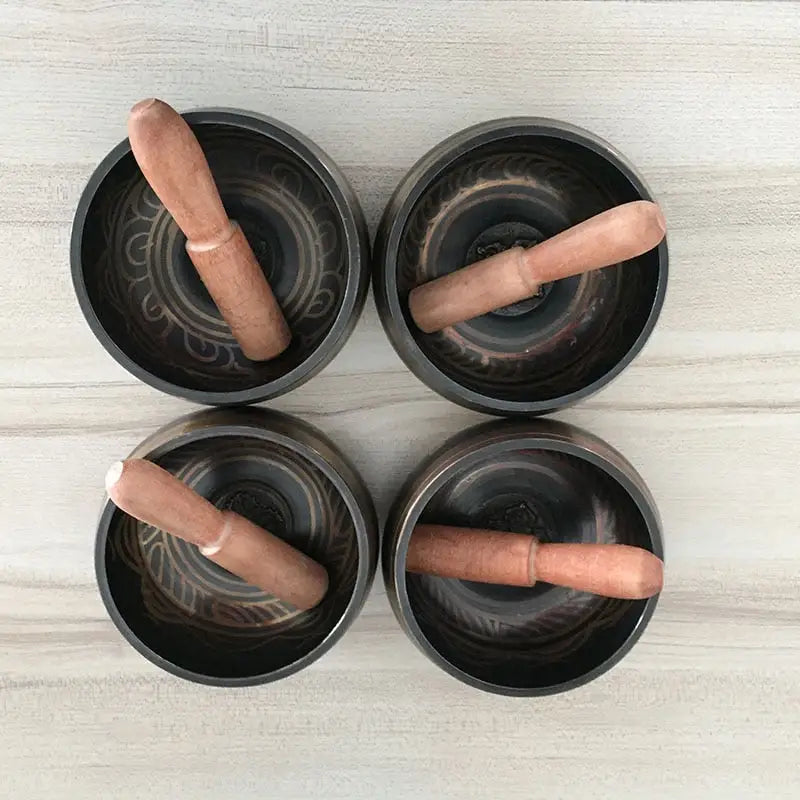 Four black ceramic bowls with hot dogs beside a Himalayan Hand-Hammered Singing Bowl