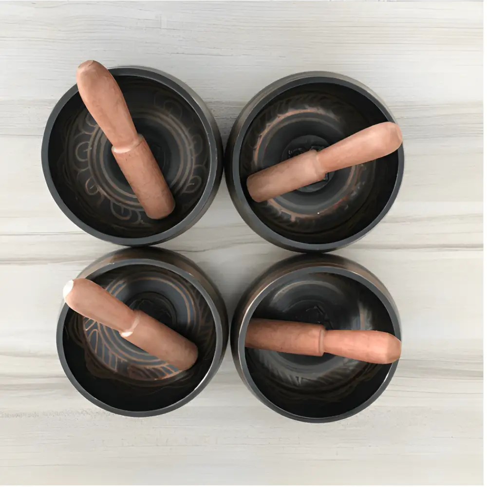 Four black ceramic mortars with wooden pestles near a Tibetan singing bowl