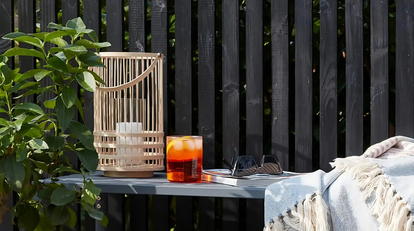 Orange-red cocktail in a glass with ice beside a bamboo lantern.