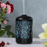 Black cylindrical essential oil diffuser featuring illuminated forest silhouette pattern