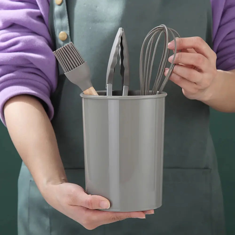 Gray cylindrical utensil holder filled with Silicone Kitchen Utensils including tongs and whisk