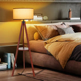 Tripod floor lamp with white drum shade and circular shelf for stylish lighting decor