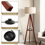 Tripod floor lamp with wooden legs, round white shade, and built-in circular shelf